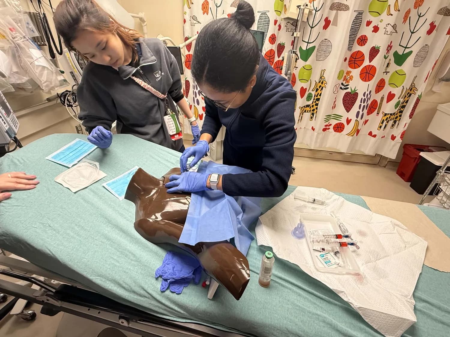 Participants practicing a clinical skill with gloves and a medical training model.